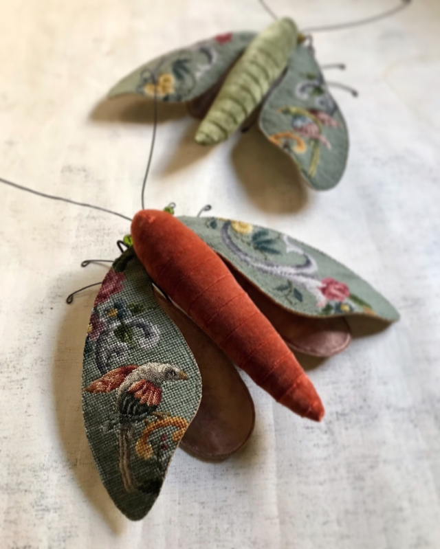 Two lush moths with animals sewn upon their wings