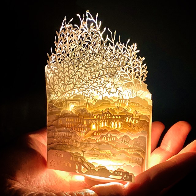 A photograph of Ayumi Shibata's white paper sculptures showcasing a miniature urban landscape with large trees