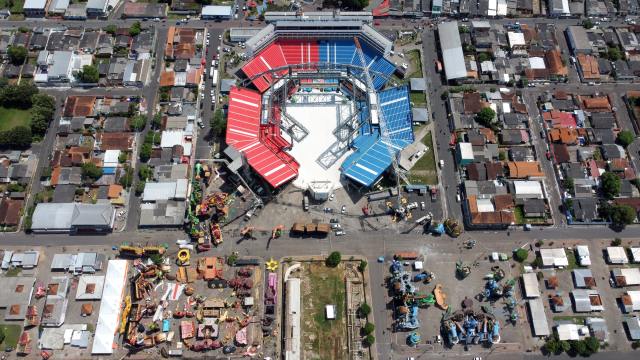 An aerial view of a city neighbourhood. At the centre is a large venue with a red and blue seats.